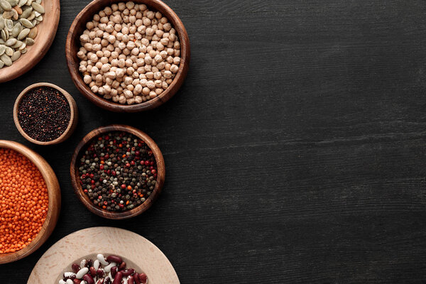 top view of black quinoa, red lentil, beans, pumpkin seeds, peppercorns and chickpea on dark wooden surface