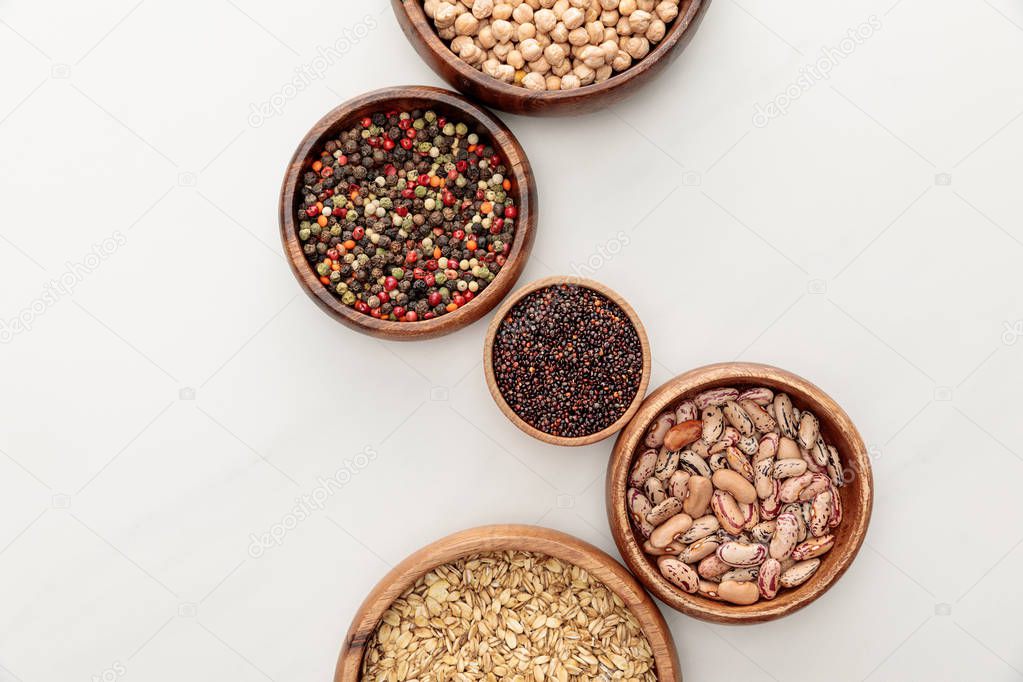 top view of wooden bowls with black quinoa, oatmeal, beans, peppercorns and chickpea on white marble surface