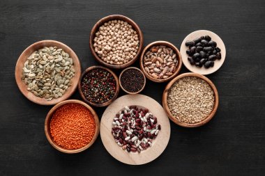 top view of various wooden plates and bowls with beans, cereals, spice and pumpkin seeds on dark wooden table clipart
