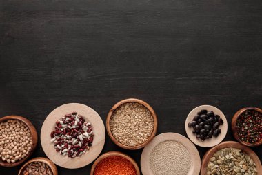 kopya alanı ile koyu ahşap yüzeyüzerinde kaselerde çiğ fasulye, tahıl, baharat ve kabak çekirdeği üst görünümü