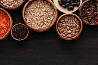 top view of raw beans, cereals and spice in bowls on dark wooden surface with copy space clipart