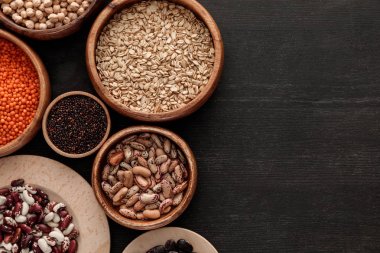 kopya alanı ile koyu ahşap yüzeyüzerinde çiğ fasulye, mercimek, yulaf ve Quinoa ile kahverengi kase üst görünümü