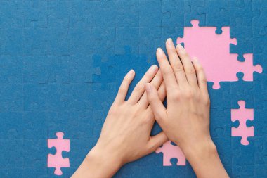 cropped view of woman covering blue jigsaw puzzle on pink background clipart