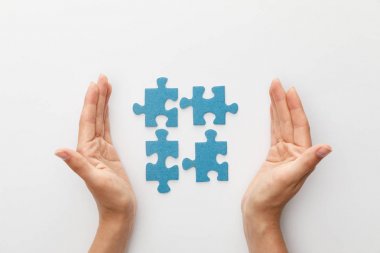 cropped view of woman hands near pieces of blue jigsaw puzzle on white background clipart