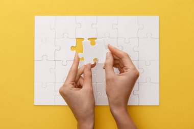 sarı arka plan üzerinde beyaz yapboz parçası tutan kadın kırpılmış görünümü