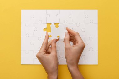 cropped view of woman holding piece of white jigsaw puzzle on yellow background clipart