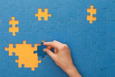 cropped view of woman putting piece of blue jigsaw puzzle on yellow background clipart