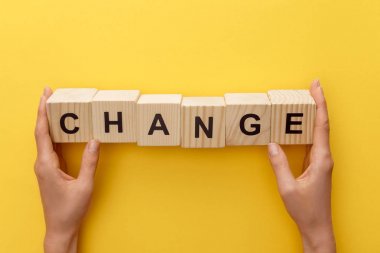 cropped view of woman holding wooden cubes with change inscription on yellow background clipart