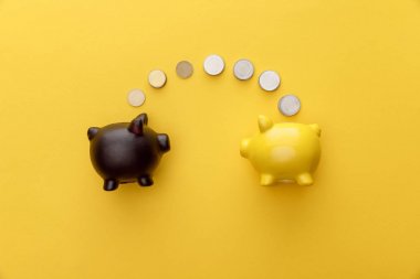 top view of piggy banks with coins on yellow background