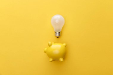 top view of piggy bank with light bulb on yellow background clipart