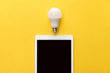 top view of light bulb and digital tablet with blank screen on yellow background clipart