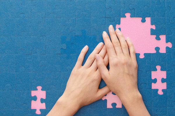 cropped view of woman covering blue jigsaw puzzle on pink background