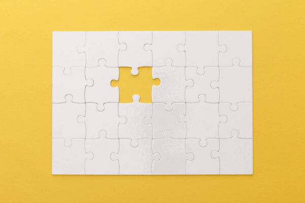 top view of white jigsaw puzzle with lost piece on yellow background
