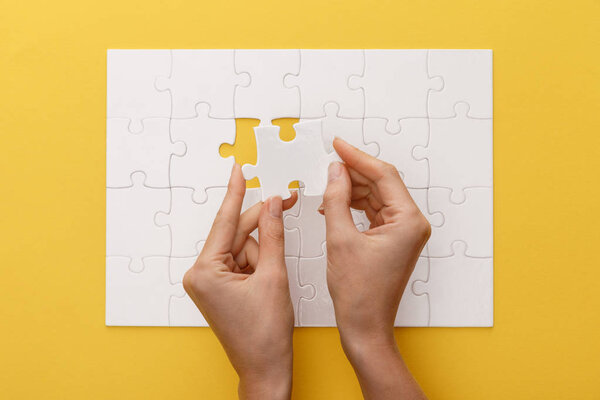 cropped view of woman holding piece of white jigsaw puzzle on yellow background