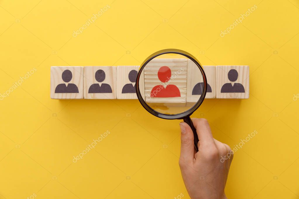 Cropped view of woman holding magnifying glass under wooden cubes with logo on yellow background