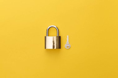 top view of padlock near key on yellow background clipart