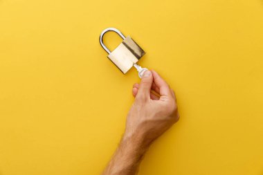 cropped view of man holding key in padlock on yellow background clipart