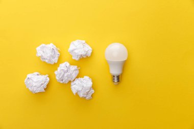 top view of light bulb near crumpled paper on yellow background clipart