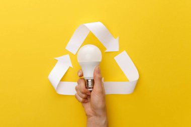 cropped view of woman holding light bulb under paper craft triangle on yellow background clipart