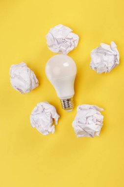 top view of crumpled paper around light bulb on yellow background clipart