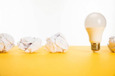 crumpled paper near light bulb on yellow surface isolated on white clipart