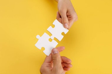 cropped view of woman and man matching pieces of white puzzle on yellow background clipart