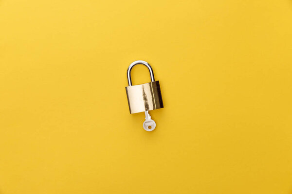 top view of key in padlock on yellow background