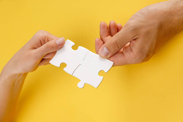 cropped view of man and woman matching pieces of white puzzle on yellow background
