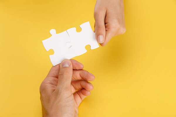cropped view of man and woman holding pieces of white puzzle on yellow background