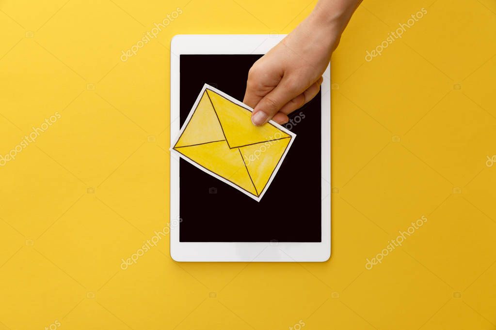 Cropped view of woman holding letter under digital tablet with blank screen on yellow background