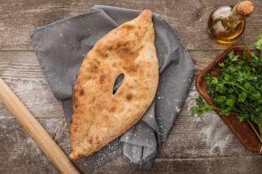 oklava, taze maydanoz ve ahşap masada zeytinyağı yakın gri havlu üzerinde lavaş ekmek üst görünümü
