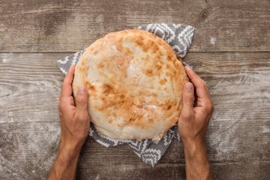 ahşap masa üzerinde desen ile gri havlu üzerinde lavaş ekmeği tutan adam kırpılmış görünümü