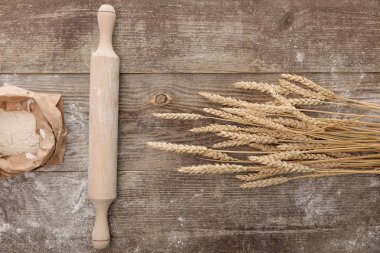 top view of wheat spikes, rolling pin and flour package on wooden table clipart