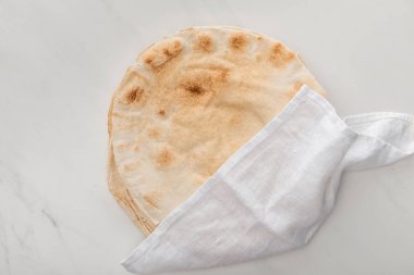 top view of flat lavash bread covered with white towel on marble surface clipart