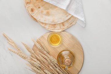 top view of lavash bread covered with white towel near cutting board with spikes and oil on marble surface clipart