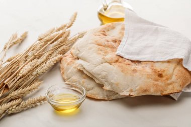 lavash bread covered with towel near spikes and oil on marble surface clipart
