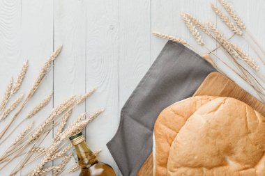 beyaz ahşap yüzeyüzerinde sivri ve zeytinyağı yakın gri havlu üzerinde lavaş ekmek üst görünümü