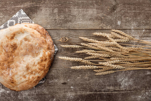 top view of lavash bread on gray towel with pattern near wheat spikes on wooden table