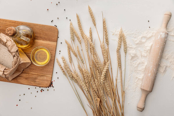 вид сверху на хлеб лаваш возле шипов и оливковое масло на белой поверхности с перцем
