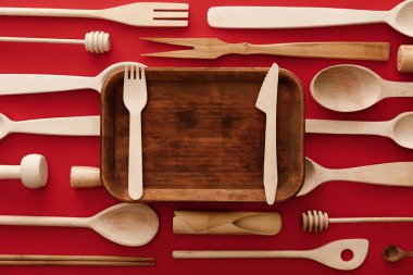top view of rectangular wooden dish with knife and fork on red background with kitchenware clipart