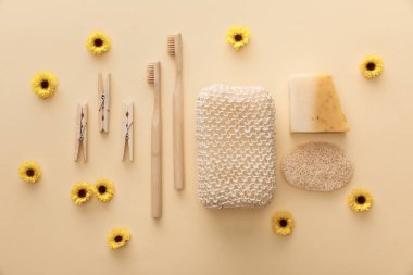 ahşap clothespins üst görünümü, diş fırçaları, banyo süngeri, doğal sabun ve çiçeklerle bej arka plan üzerinde loofah