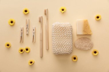top view of wooden clothespins, toothbrushes, bath sponge, natural soap and loofah on beige background with flowers clipart