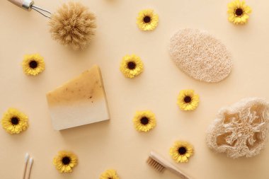 loofah üst görünümü, pamuklu bezler, vücut fırçası, diş fırçası ve çiçeklerle bej arka plan üzerinde sabun parçası
