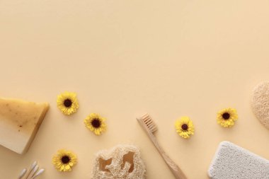 loofah üst görünümü, pamuklu bezler, pomza taşı, diş fırçası ve çiçeklerle bej arka plan üzerinde sabun parçası