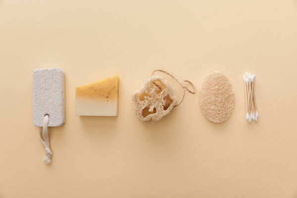 top view of natural soap near cotton swabs, loofah and pumice stone on beige background