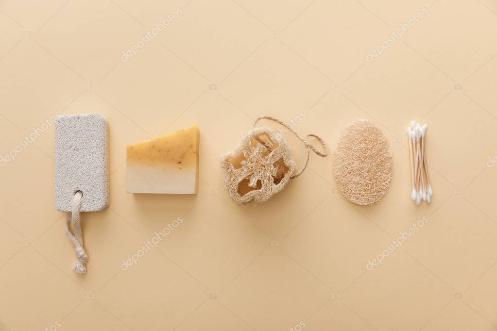Top view of natural soap near cotton swabs, loofah and pumice stone on beige background