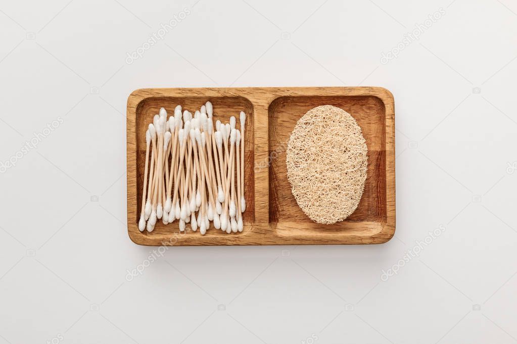 top view of wooden dish with cotton swabs and loofah on white background