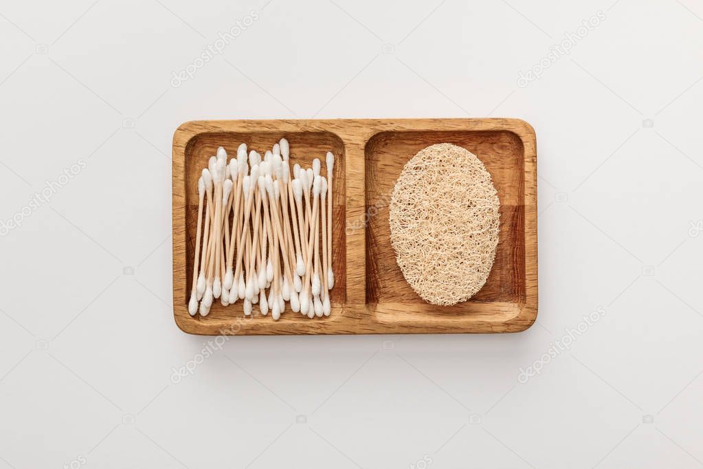 Top view of wooden dish with cotton swabs and loofah on white background