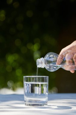 Plastik şişeden temiz suyu cama döken insan görüntüsü.