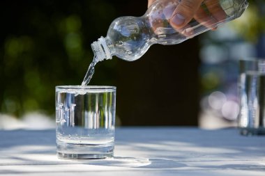 Plastik şişeden temiz suyu cama döken insan görüntüsü.
